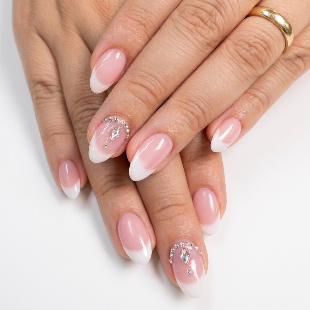 Soft pink almond nails with white French tips and crystal accents